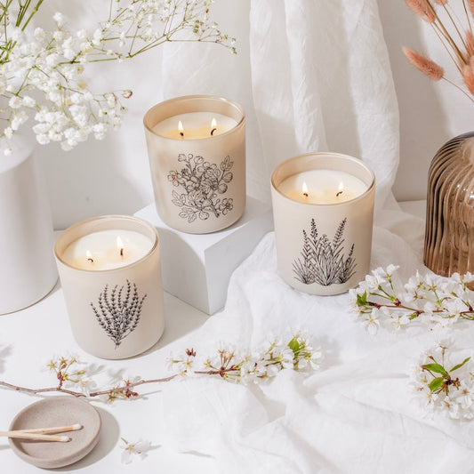 Candles with floral designs on a white surface with flowers and a vase.