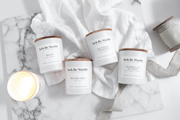 Jack Be Nimble soy candles from the Classics Collection, including Woodland, Proof, Southern Sunshine, Cotillion, and Georgia On My Mind, displayed on white linen and marble for a clean, elegant presentation.