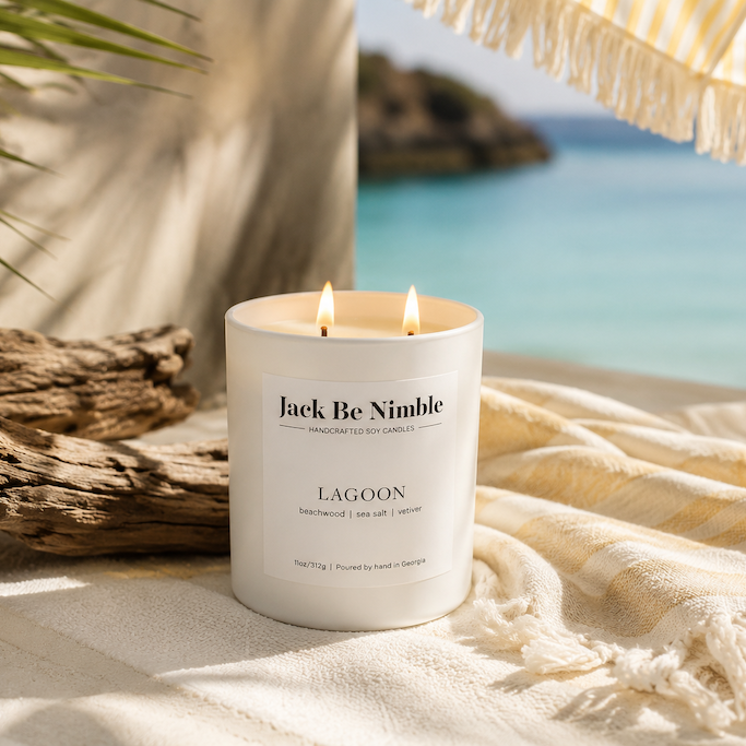 Candle labeled 'Jack Be Nimble' on a sandy surface with a beach background
